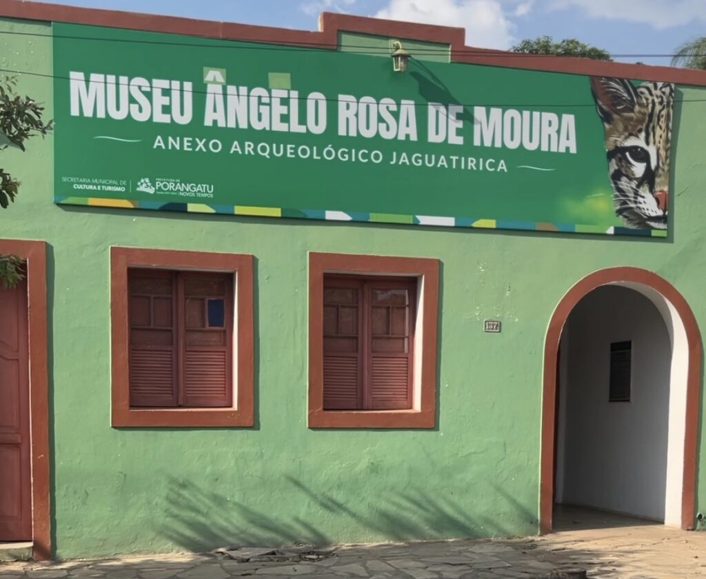 Fachada de prédio histórico pintado de verde, com duas janelas de madeira e uma porta em arco à direita. Acima da fachada há um grande banner verde com o nome “Museu Ângelo Rosa de Moura – Anexo Arqueológico Jaguatirica” e a imagem de uma jaguatirica.