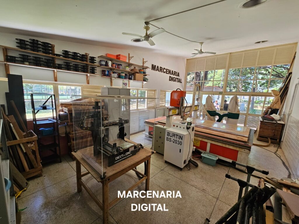 Sala com dias máquina CNC prateleiras com isumos para marcenaria, porta ao fundo que acessa o pátio externo