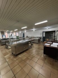 Sala de necropsia do antigo IML de Curitiba, localizada no Museu Paranaense de Ciências Forenses. Nela é possível ver 4 mesas de necropsia de inox, em uma sala com piso de cerâmica marrom e o teto e paredes brancas. No lado direito é possível ver uma mesa de madeira e uma cadeira. Ao fundo existe uma porta que leva até a sala das câmaras frias.