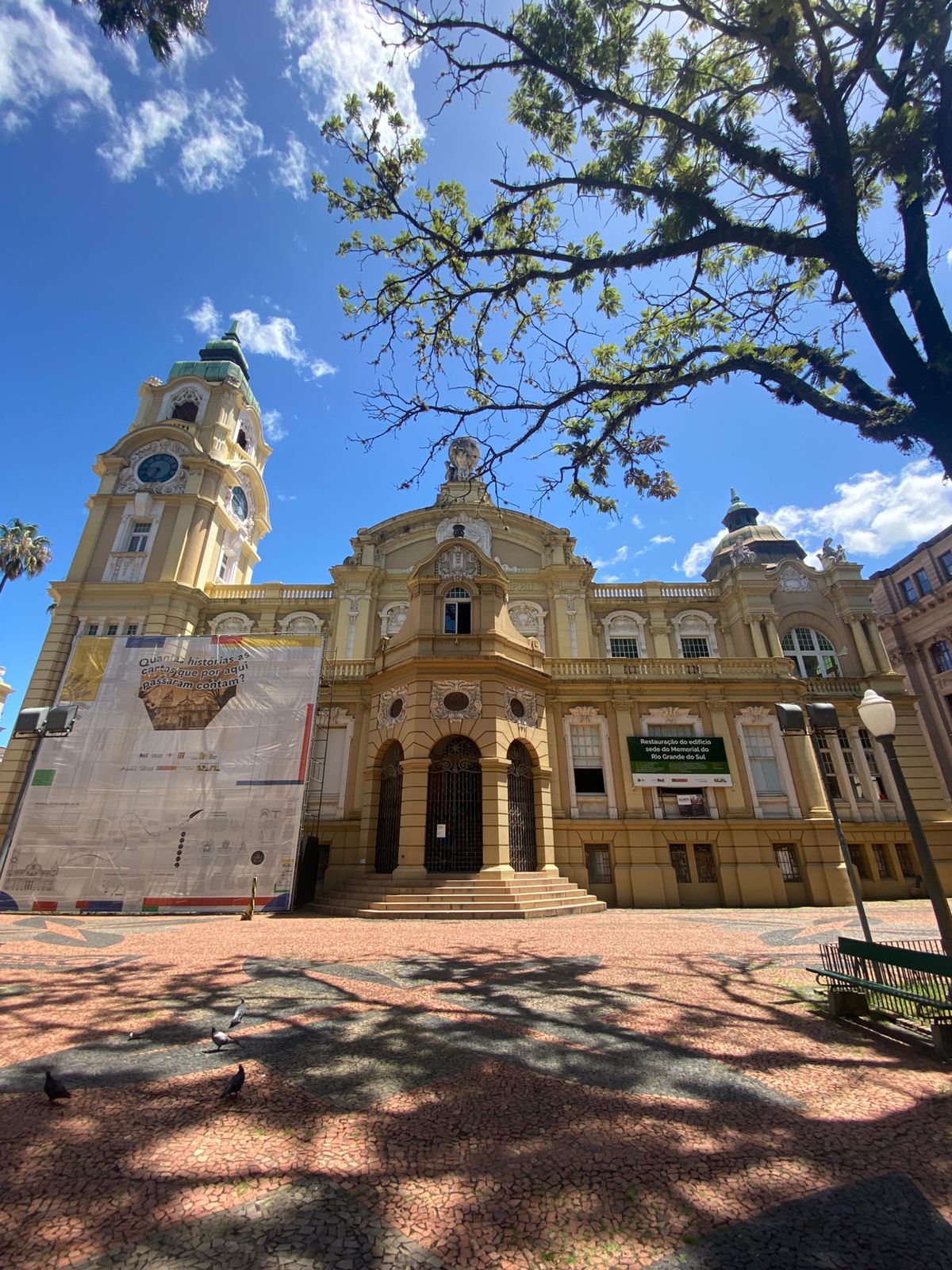 Prédio histórico do Memorial do Rio Grande do Sul, na Praça da Alfândega, em Porto Alegre. A fachada apresenta conjunto escultórico com atlas sustentando o globo, figura feminina lendo uma carta e torre com relógio.