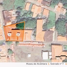 Imagem aérea do Museu de Alcântara, com indicação do n°1 e n°2 para os sobrados que fazem parte do conjunto do Museu. Os dois edifícios estão localizados em uma rua estreita, cercados por construções com telhados cerâmicos e vegetação abundante. A imagem inclui a legenda com a identificação das edificações, no canto inferior direito a escala gráfica e, na parte superior esquerda, uma seta indicando o ponto cardeal norte.