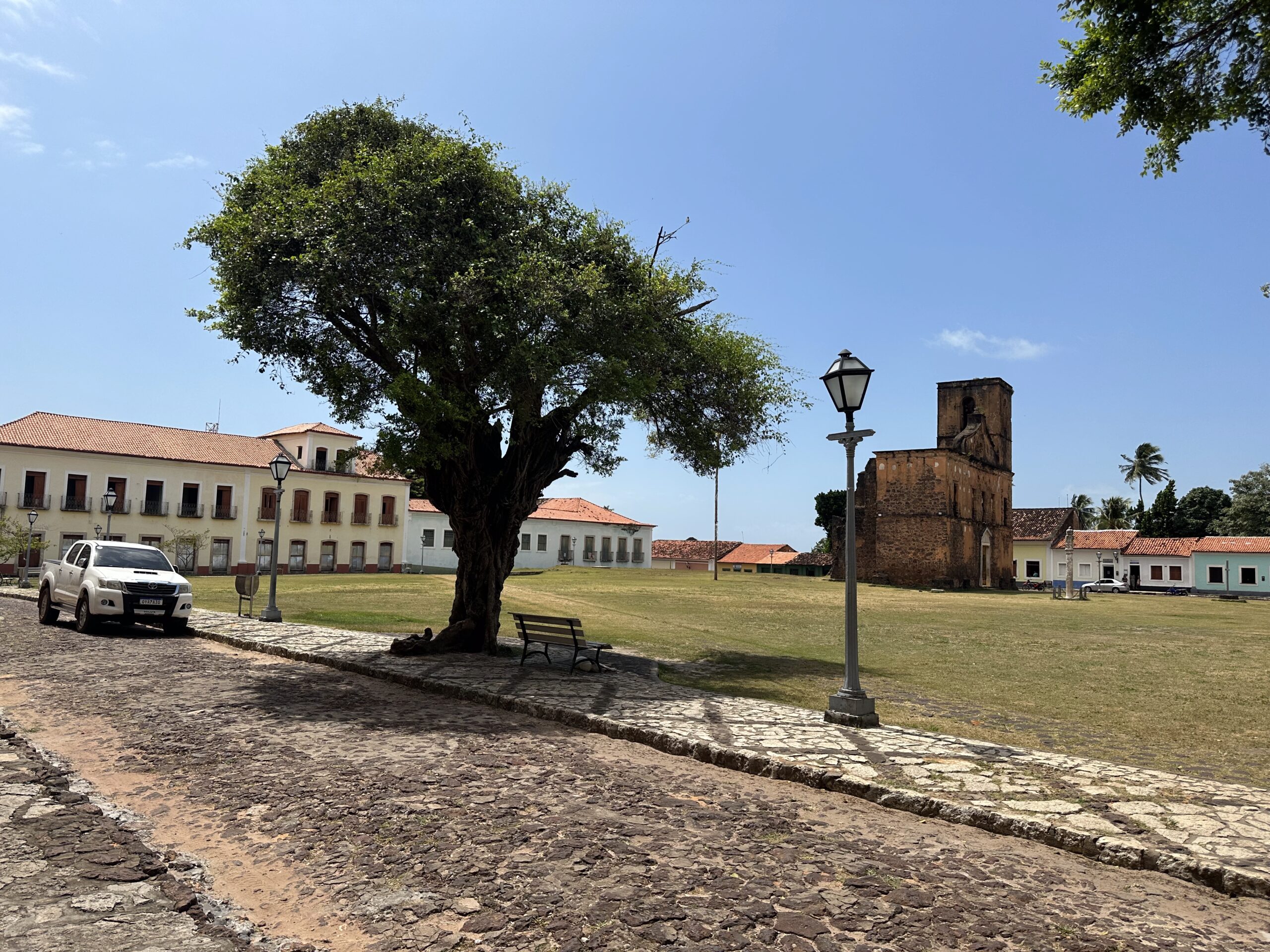 Imagem de um caminho de pedras com árvores e, ao fundo, uma ampla praça. À esquerda, um conjunto de dois edifícios que é o Museu de Alcântara.