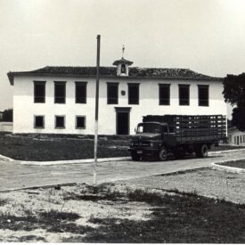 Fotografia histórica em preto e branco do museu retratando o edifício de dois andares, com telhado de quatro águas e várias janelas. No centro do telhado, há uma pequena mansarda. Em frente ao prédio, um caminhão está estacionado sobre a via. A área ao redor apresenta partes gramadas e trechos de terra.