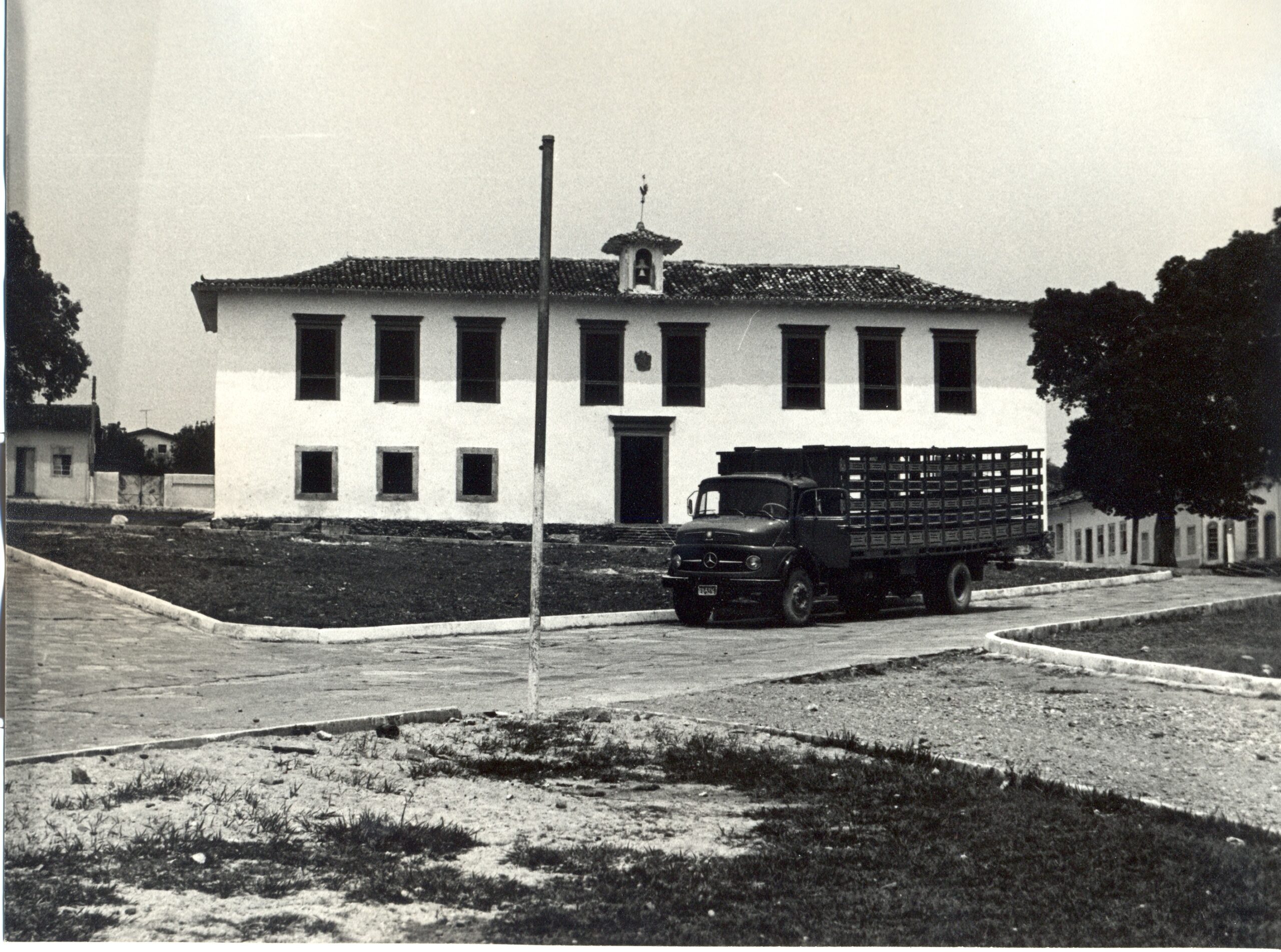 Fotografia histórica em preto e branco do museu retratando o edifício de dois andares, com telhado de quatro águas e várias janelas. No centro do telhado, há uma pequena mansarda. Em frente ao prédio, um caminhão está estacionado sobre a via. A área ao redor apresenta partes gramadas e trechos de terra.