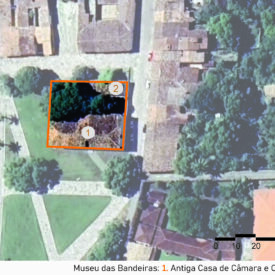 Vista aérea do museu localizado em uma área urbana com várias casas e árvores. No centro da imagem, um quadrado laranja destaca a propriedade que contém um edifício, um anexo e áreas verdes ao redor. Dentro do quadrado, há dois círculos numerados: o número 1, Antiga Casa de Câmara e Cadeia, e o número 2, anexo, sobre a área verde com árvores. A imagem inclui a legenda com a identificação das edificações, no canto inferior direito a escala gráfica e, na parte superior esquerda, uma seta indicando o ponto cardeal norte.