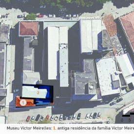 Imagem aérea do museu, localizado em um quarteirão urbano com vários edifícios. O conjunto está destacado por um polígono laranja, o número 1 indica o Museu, antiga residência da família Victor Meirelles, e o número 2, seu Anexo. A imagem inclui a legenda com a identificação das edificações, no canto inferior direito a escala gráfica e, na parte superior esquerda, uma seta indicando o ponto cardeal norte.