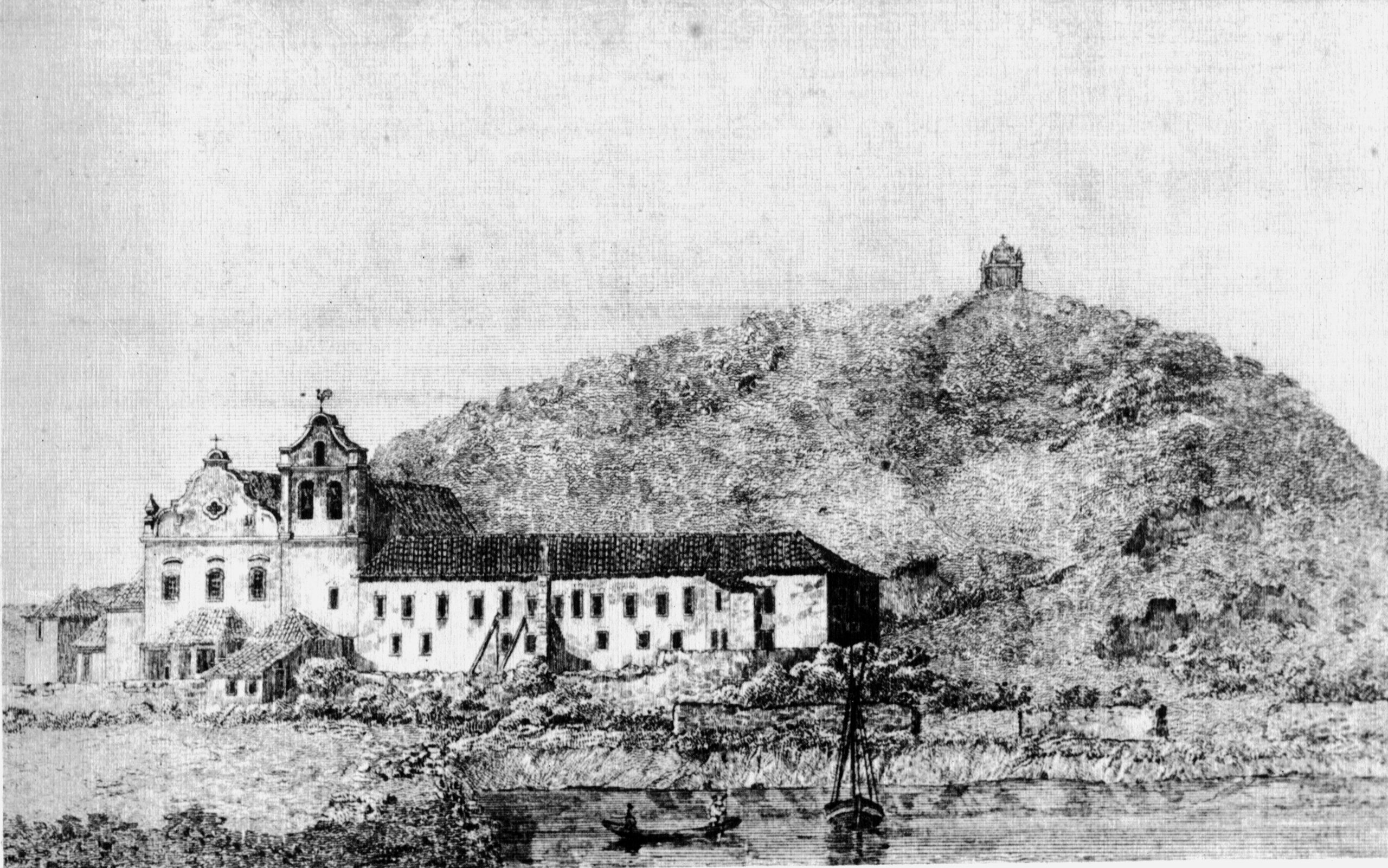 Fotografia histórica em preto e branco do museu. O conjunto de edifícios é composto por volumes de diferentes alturas e formatos. À esquerda da imagem, observa-se a igreja com a torre lateral e, à direita, uma edificação retangular de dois pavimentos com diversas janelas distribuídas ao longo da fachada. Ao fundo, observa-se uma colina coberta por vegetação.