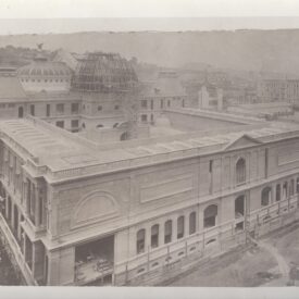 Fotografia antiga em tons de sépia, retratando a construção do museu, com destaque para a estrutura de cúpula parcialmente concluída no centro. Nota-se detalhes ornamentais e várias janelas distribuídas pela fachada. Há andaimes visíveis ao redor da cúpula e em outras partes do prédio, indicando que a obra ainda está em andamento.